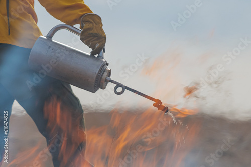 Close-up of a firefighter lighting grass on fire using a drip torch  photo