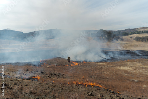 A firefighter lights grass on fire using a drip torch 