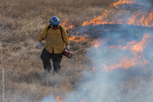 A firefighter lights grass on fire using a drip torch 