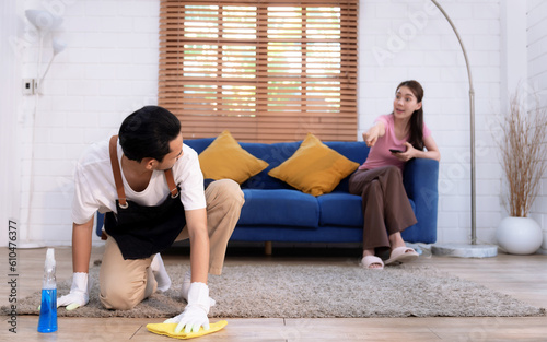 Asian man cleaning living room alone, While the lazy girlfriend doesn't help him.