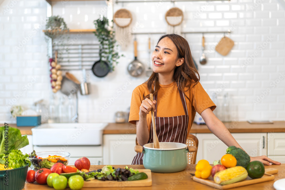 Young woman standing near stove and cooking.Happy woman looking and smelling tasting fresh delicious from soup in a pot with steam at white interior kitchen