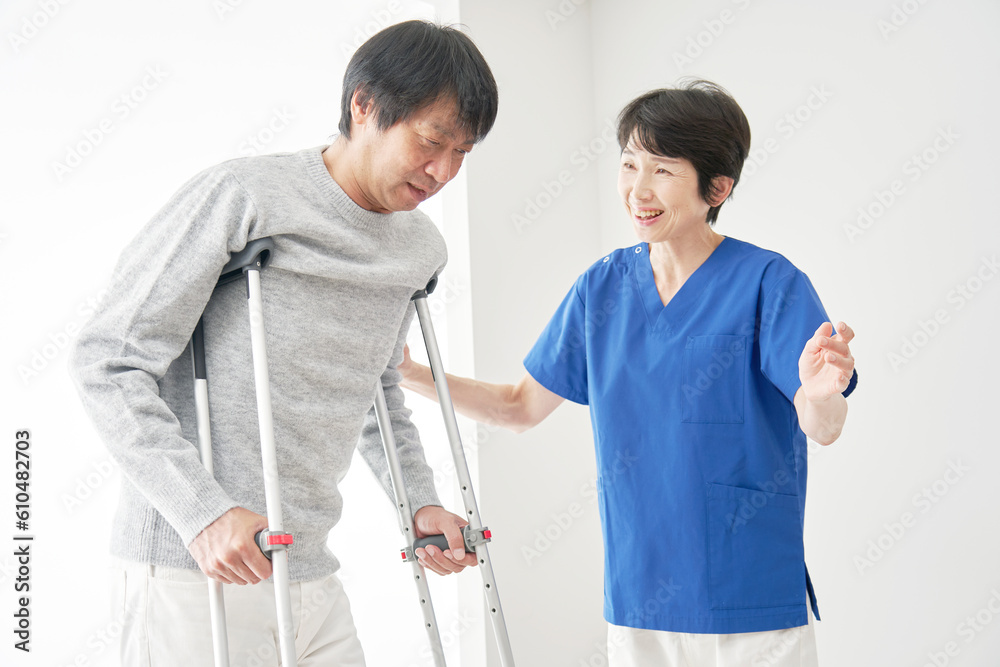 松葉杖を使って歩くリハビリをする中年男性 松葉杖を使って歩くリハビリをする中年男性