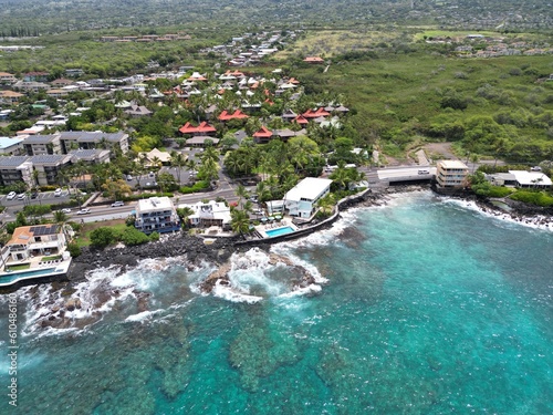 View of coastal Kailua-Kona on the Big Island of Hawai'i. Aerial drone looking along the coast with palm trees, houses, condominiums, and blue and green waters with volcanic rock and coral. photo