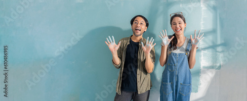Cheerful funny Asian marry couple playful show dirty colour splash hand standing together near new painting wall new renovation home relocation house,smiling couple playing colour take a break