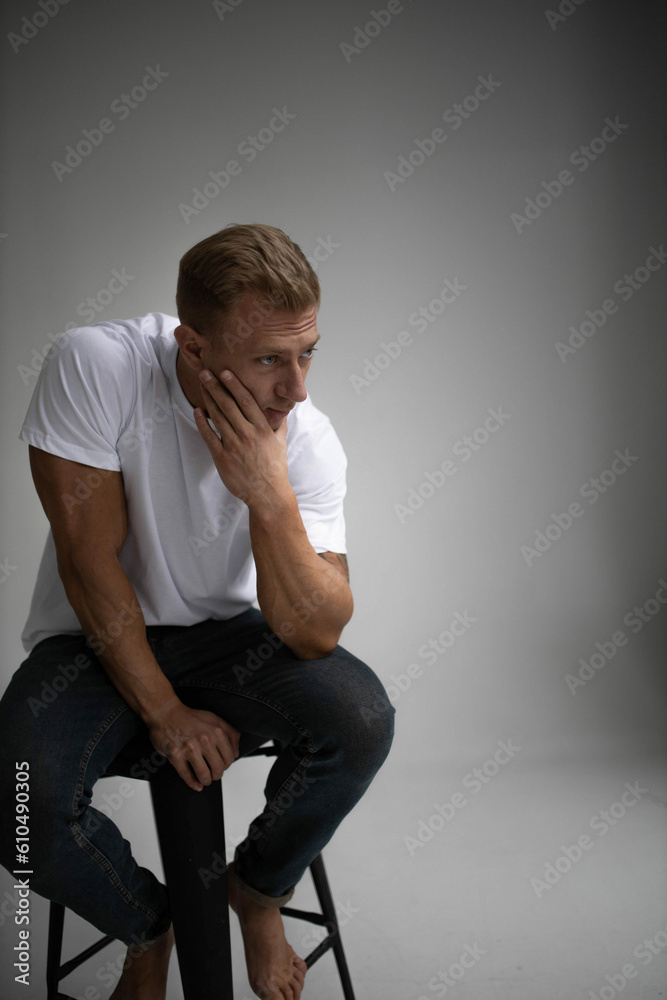 handsome male actor model posing sitting on armchair in studio in white t-shirt. handsome male actor model posing sitting on armchair in studio in white t-shirt.