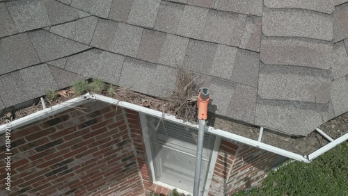 Cleaning out dirty, blocked gutters from the ground, with a plastic scoop on a pole.