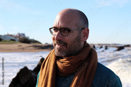 homem adulto sorrindo, em viagem turística pelo litoral, no frio do inverno no extremo da América do Sul usando óculos e manta. photo