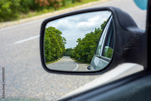Side view mirror of a two lane road in the forest