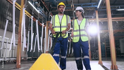 Assiduous Worker man and woman talking and pushing hand pallet truck while working in heavy manufacturing. Industry and Factory plant. photo