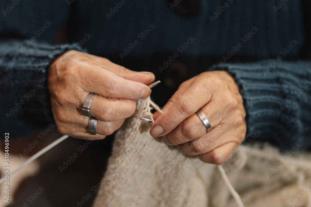 Mujer latina, adulto mayor , feliz y concentrada, en la sala de casa usando unos palitos de tejer y lana de oveja, concepto de vida cotidiana tradicional, tejedora tradicional, enfoque selectivo.