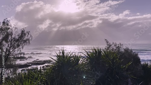 Picturesque beach in early morning - backlit. Rays filter through grey clouds