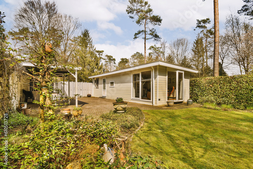 a small house in the middle of a garden with green grass and trees surrounding it is surrounded by white clouds