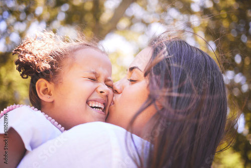 Mother, child and kiss cheek in nature, funny and bonding in summer garden on holiday. Mom kissing happy girl for love, affection and care of enjoying freedom of quality time together outdoor in park #610521914