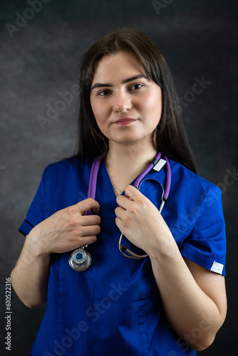 beautiful female doctor or medical student  in blue uiform with stethoscope against dark background photo