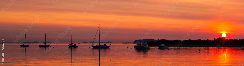Sunrise behind silhouette sailboats moored on the Neponset River under an orange sky in Dorchester, Boston