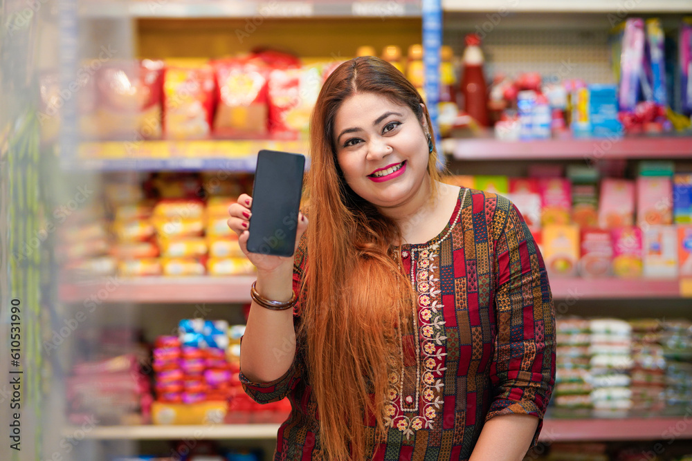 Indian woman showing smartphone screen at grocery shop.