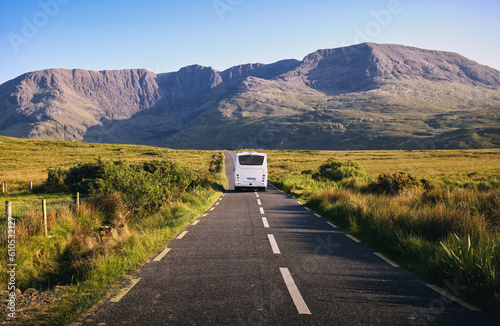 Beautiful landscape scenery with white bus driving on empty scenic road trough nature with mountains in the background at county Mayo, Ireland