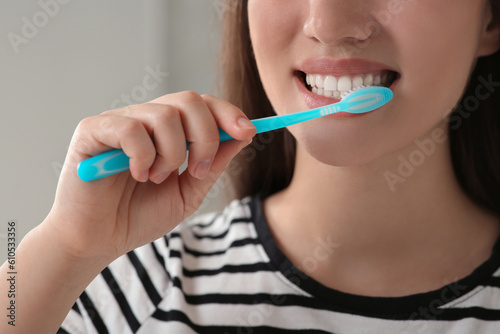 Woman brushing her teeth with plastic toothbrush indoors, closeup