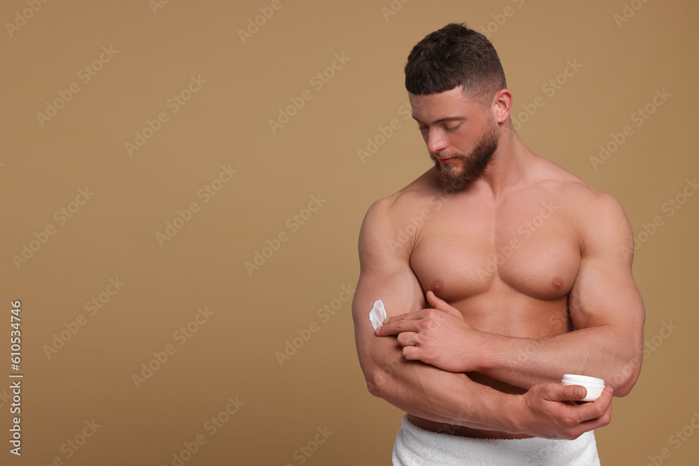 Handsome man applying body cream onto his arm on pale brown background, space for text