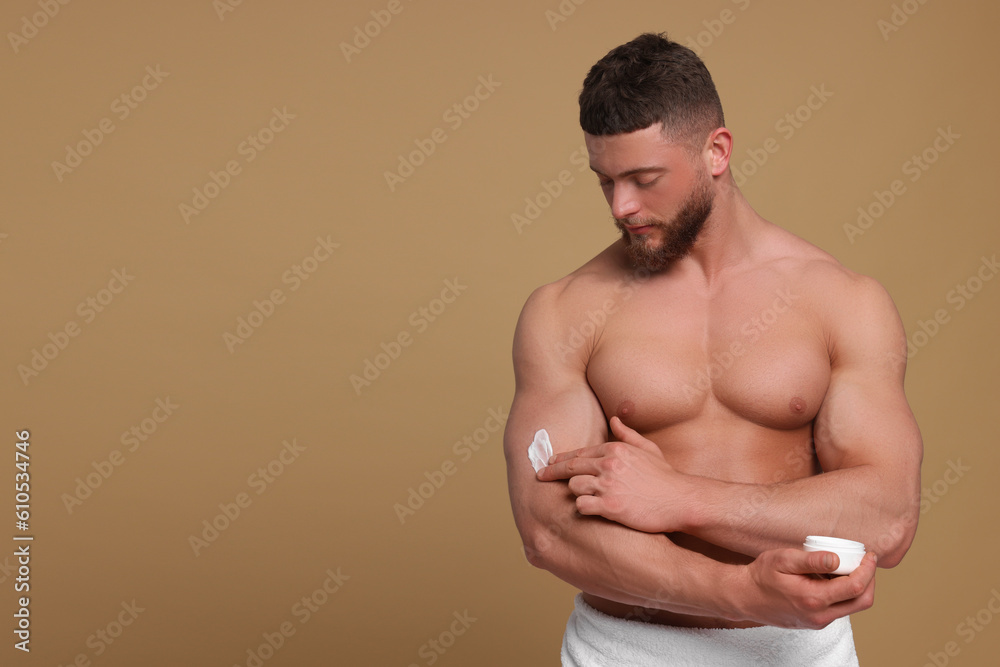 Handsome man applying body cream onto his arm on pale brown background, space for text Handsome man applying body cream onto his arm on pale brown background, space for text