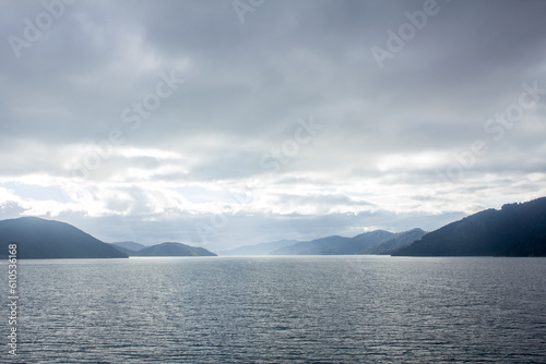 View north through Queen Charlotte Sound, ferry from Picton, Marlborough on Cook Strait to Wellington, South and North Island, New Zealand, NZ with bright sun, grey and white clouds and islands