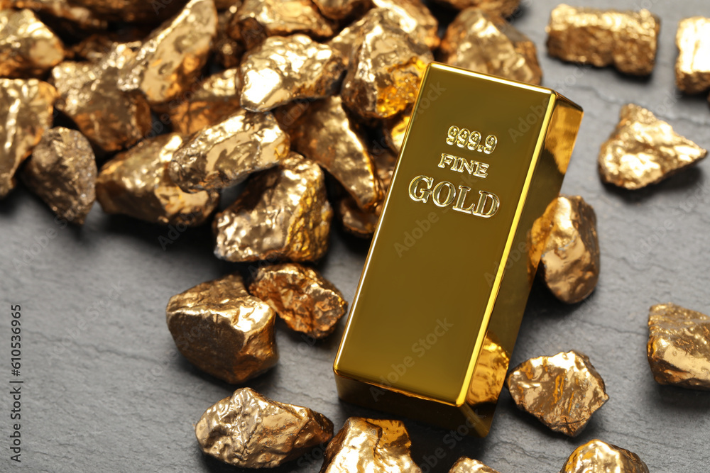 Gold ingot and nuggets on grey table, closeup Gold ingot and nuggets on grey table, closeup
