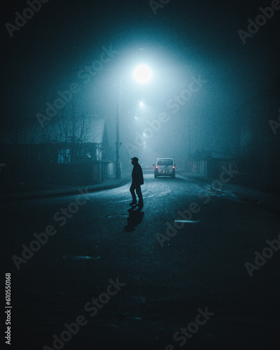 Fotografia A lone figure in a misty night, illuminated by street light.