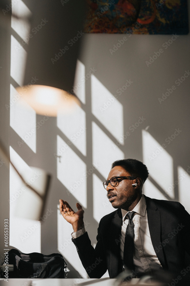 Mature businessman gesturing and talking through wireless in-ear headphones at office Mature businessman gesturing and talking through wireless in-ear headphones at office