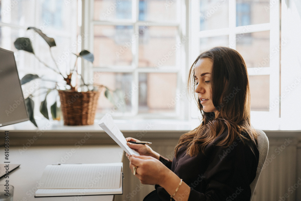 Side view of businesswoman examining document sitting at office Side view of businesswoman examining document sitting at office