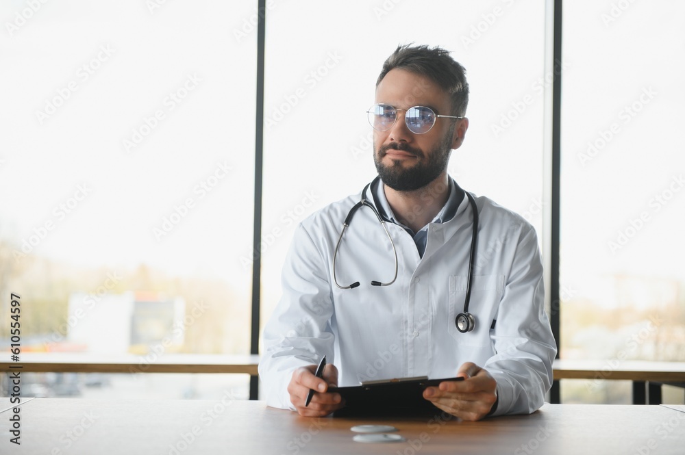 Doctor man sitting at the desk at his working place. Perfect medical service in clinic. Portrait of a handsome young doctor. Doctor man sitting at the desk at his working place. Perfect medical service in clinic. Portrait of a handsome young doctor.