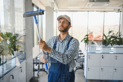 Young indian man washing window in office