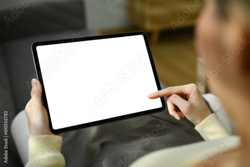 Closeup view young woman holding digital tablet with blank desktop while sitting on a sofa at home
