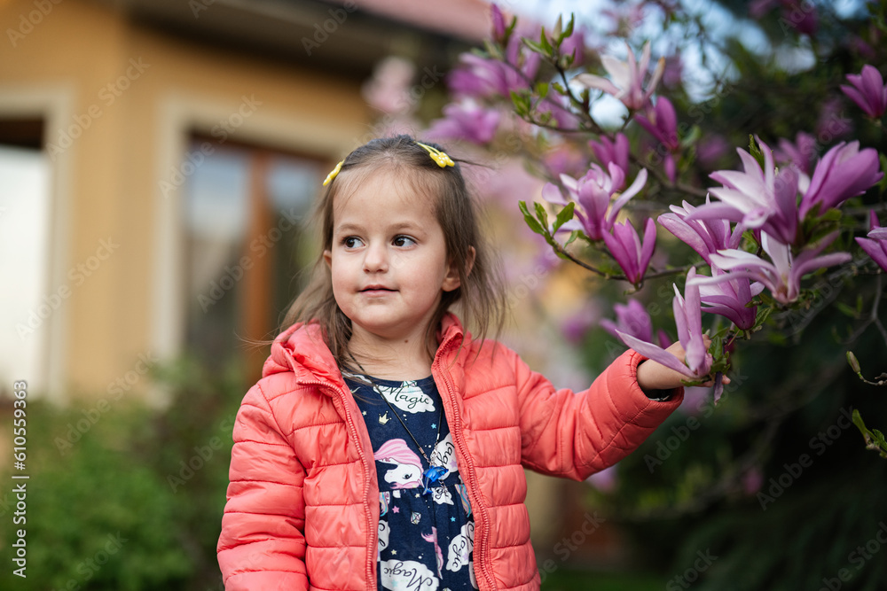 Baby girl in pink jacket enjoying nice spring day near magnolia blooming tree. Springtime activities. Baby girl in pink jacket enjoying nice spring day near magnolia blooming tree. Springtime activities.