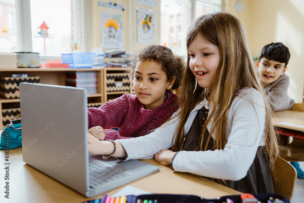 Schoolgirls using laptop together at desk in classroom Schoolgirls using laptop together at desk in classroom