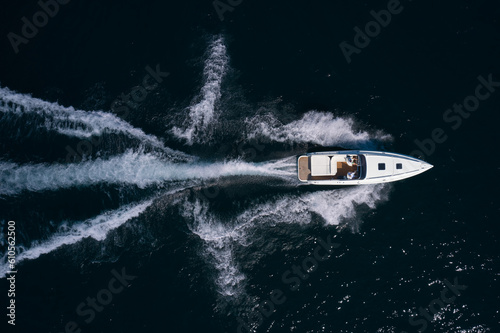 White big super speedy boat with people moving fast on dark water, top view.