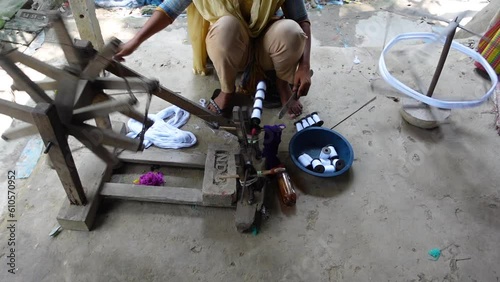 Woman spinning cotton thread by hand outside her house. The yarn is twisted into a reel through a process to make cloth.  photo