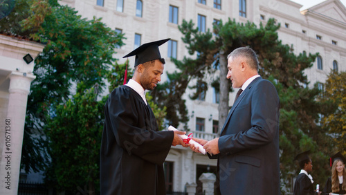 Fotografie In front of the camera mature man college professor giving diploma to his gradua