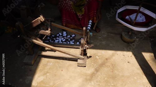 Woman spinning cotton thread by hand outside her house. The yarn is twisted into a reel through a process to make cloth.  photo