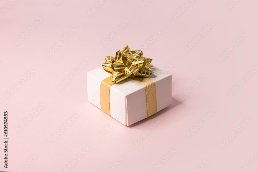 Fototapeta premium One white gift box with golden ribbon on pink background still life.
