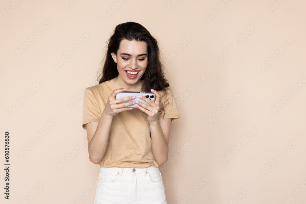 Happy attractive woman joying win in video game on smartphone, isolated over beige background Happy attractive woman joying win in video game on smartphone, isolated over beige background