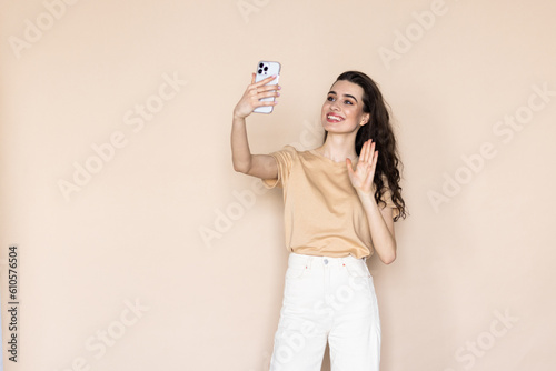 Young woman on a beige background waving her hand at the phone talking via video call