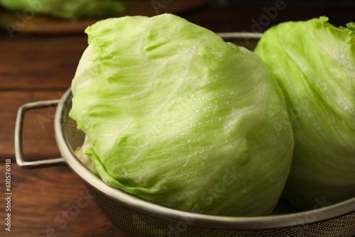 Colander with fresh green wet iceberg lettuce heads on wooden table, closeup