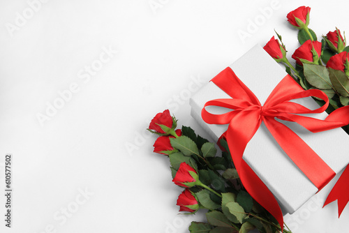Beautiful gift box with bow and red roses on white background, above view. Space for text