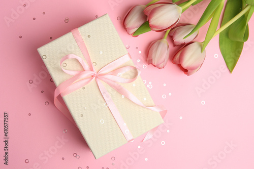 Beautiful gift box with bow, tulips and confetti on pink background, flat lay © New Africa