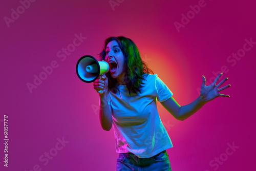 Portrait of serious young woman, girl shouting via loudspeaker over pink background in neon light. Concept of emotions, breaking news, Black Fiday, Big sales photo