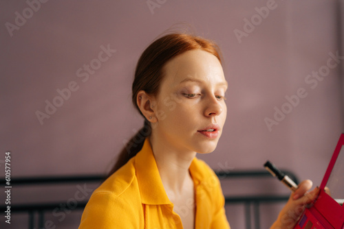 Closeup face of pretty redhead young woman applying foundation on face to correct skin and hide pimples near lips in bedroom. Red-hared female doing makeup putting base tone cream using concealer.