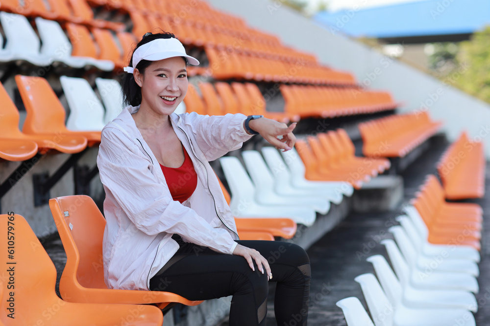 Portrait of happy and excited young female asian sport fan cheering and watching the match with her finger pointing, she sitting amongst the rows of empty seats on stadium while celebrate winner team Portrait of happy and excited young female asian sport fan cheering and watching the match with her finger pointing, she sitting amongst the rows of empty seats on stadium while celebrate winner team