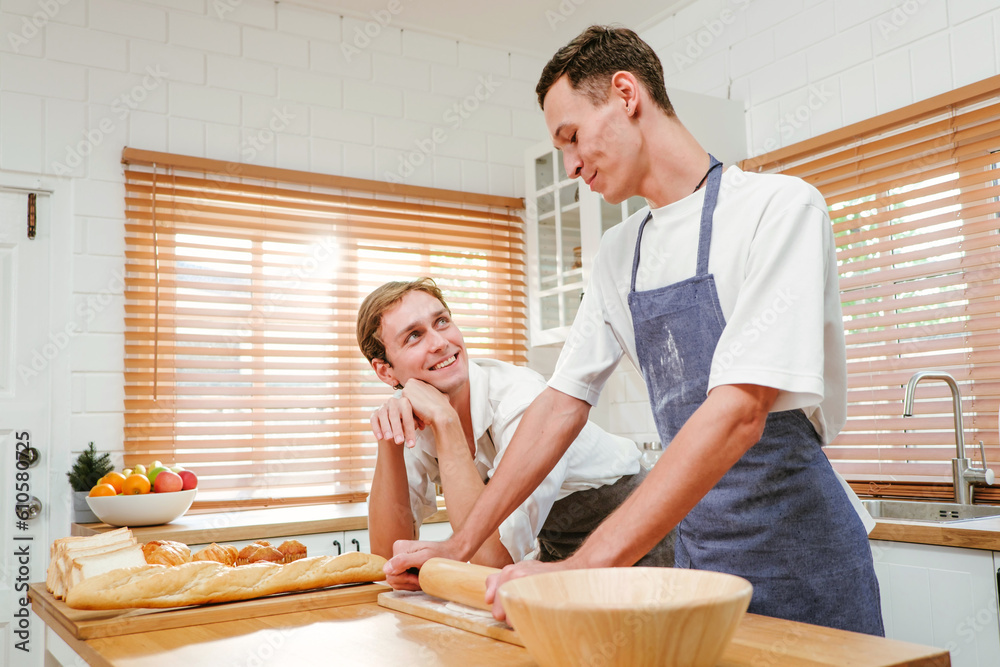 Fototapeta premium Happy Caucasian gay couple cooking together in the kitchen while watching each other with fun and a smile. Man standing by boyfriend preparing food at home. LGBT couple concept.