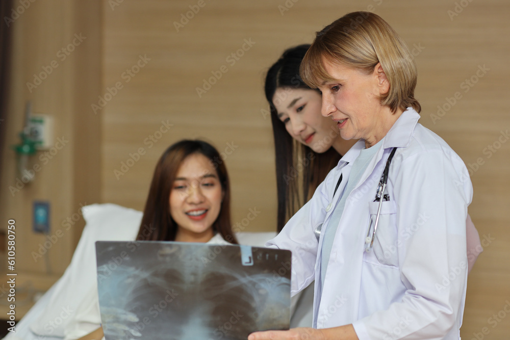 Female doctor greeting and showing happy patient and her friend with x-ray film after surgery in hospital room. Medical and insurance concept. Female doctor greeting and showing happy patient and her friend with x-ray film after surgery in hospital room. Medical and insurance concept.