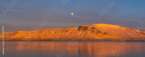 Billede på lærred Orange snowy mountains of Videy Island illuminated by light of the evening sun with its symmetrical reflection in the water of the Atlantic Ocean with the red full moon in the background